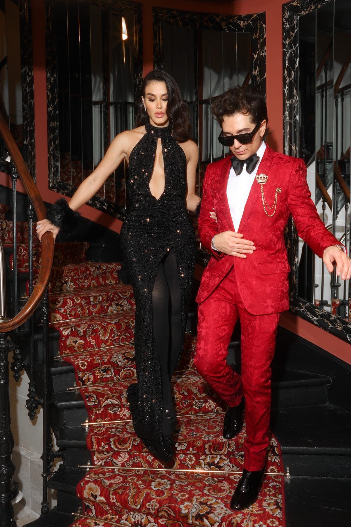 Couple in a red tuxedo and black sequin gown coming down the staircase, private birthday party in Paris